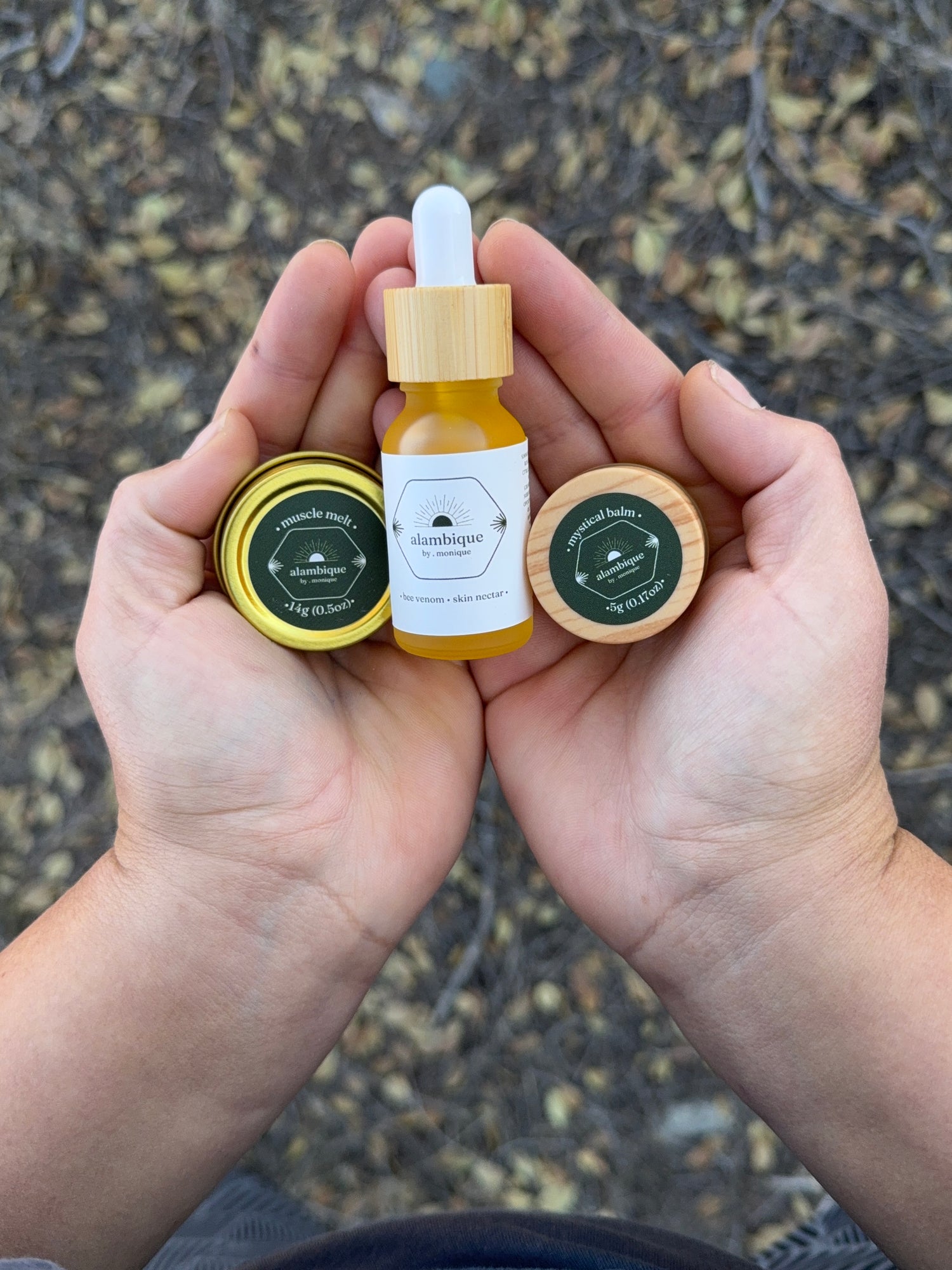 Hands holding alambique bee venom skincare set with wild rosehip outdoors