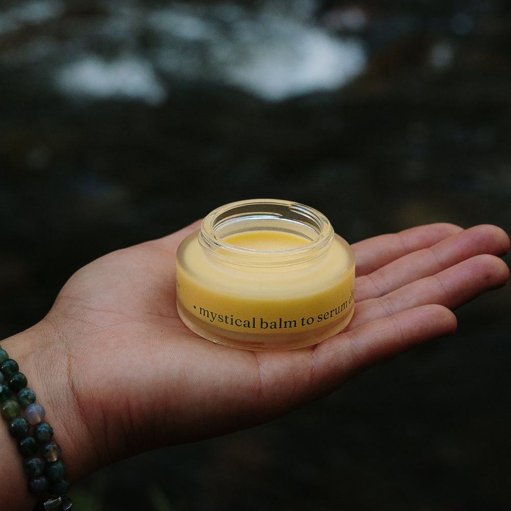 mystical balm to serum elixir next to a stream with a cap off