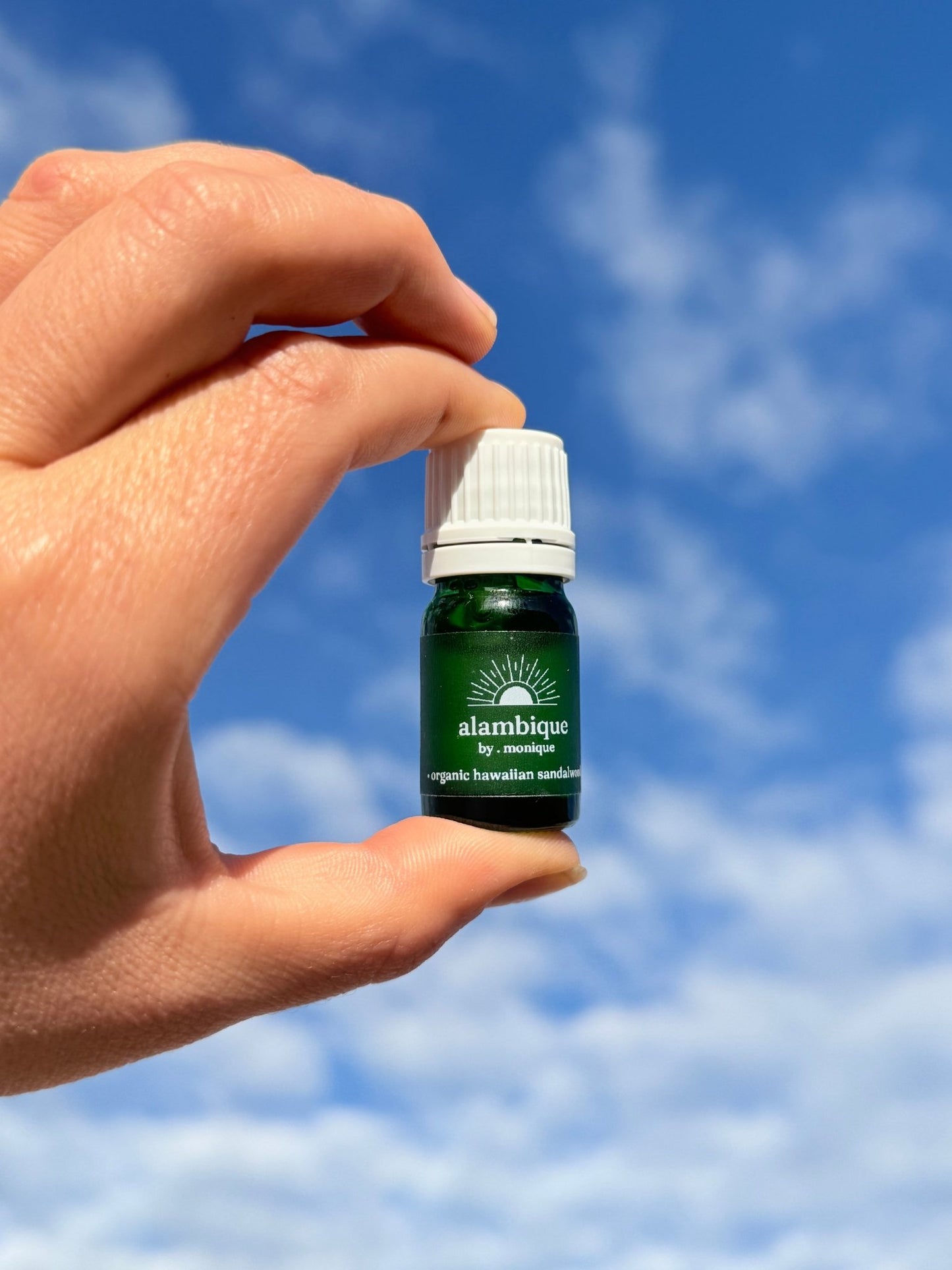 organic royal Hawaiian sandalwood essential oil •the • alambique. green essential oil bottle in sky with white cap
