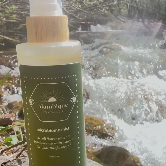 Certified organic barrier repair face mist by the alambique, containing neroli and frankincense hydrosols, set against a pristine flowing river.
