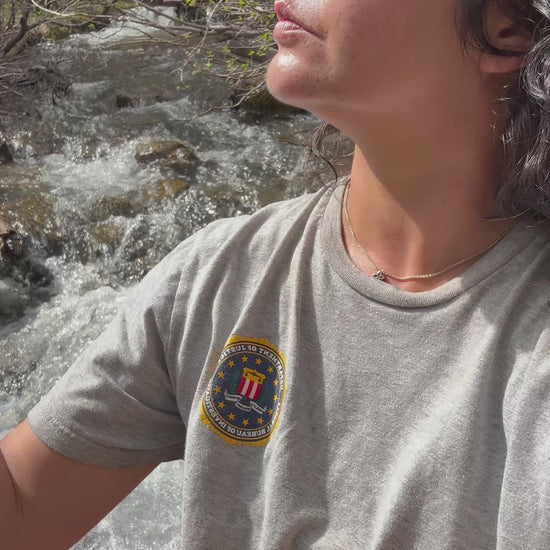A woman closes her eyes to enjoy a refreshing mist of the•alambique organic microbiome facial toner while sitting by a sunlit mountain river stream.