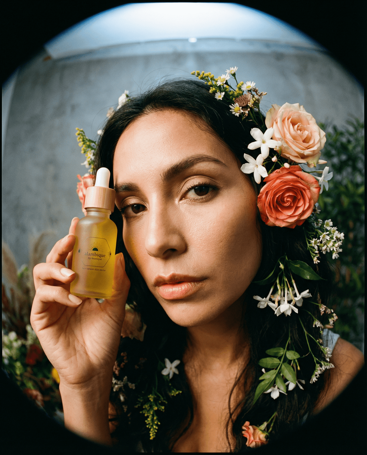the best ethical bee venom skin serum held up to a Hispanic woman's face with a floral headband